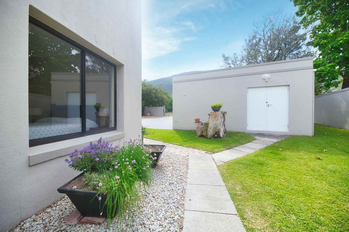 A well-maintained rear garden area featuring a paved walkway leading to a detached garage, complemented by neat landscaping and gravel beds.