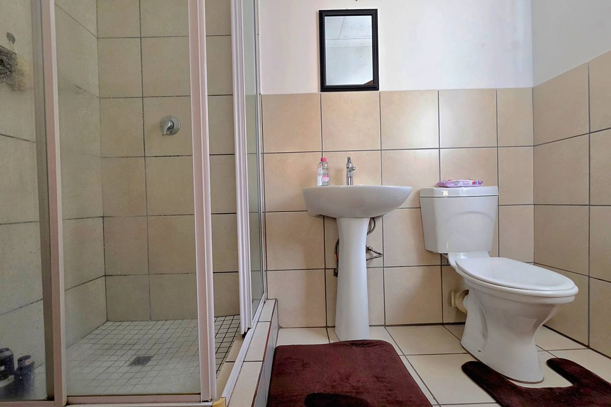 A functional bathroom featuring a glass-enclosed shower, pedestal basin, and toilet with neutral wall and floor tiling.