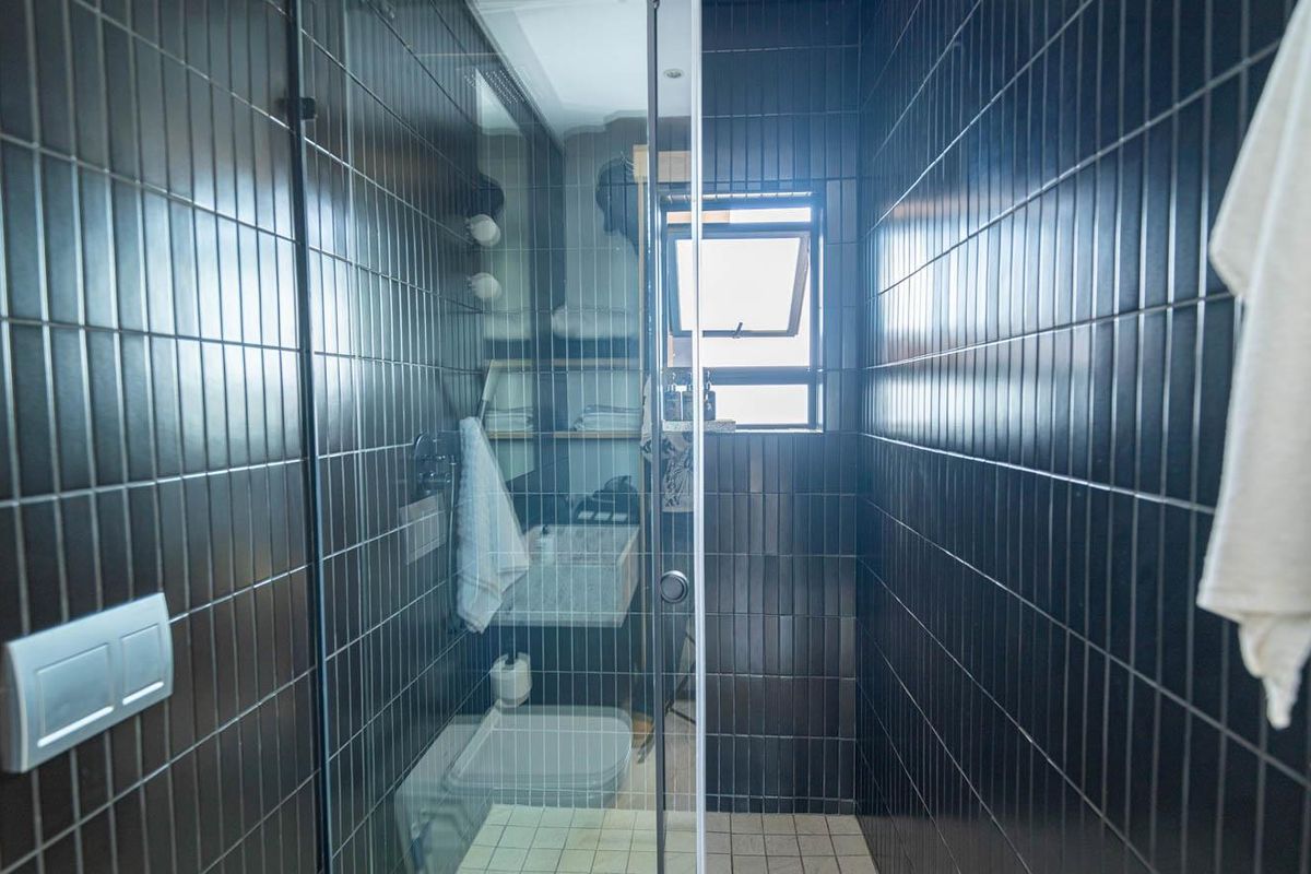 Modern bathroom featuring dark vertical wall tiles, a glass-enclosed shower, and a wall-mounted toilet with a sleek flush plate.