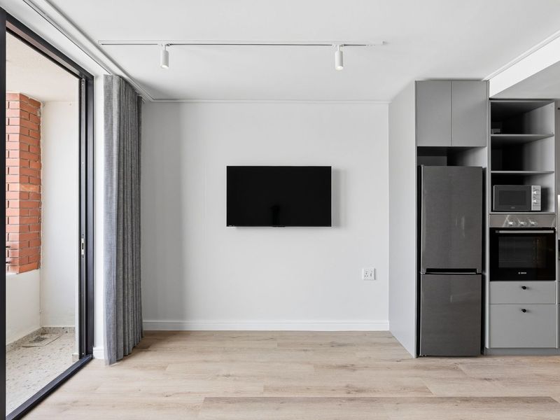 Modern open-plan living area featuring sleek grey cabinetry, integrated kitchen appliances, track lighting, and direct access to a private balcony.
