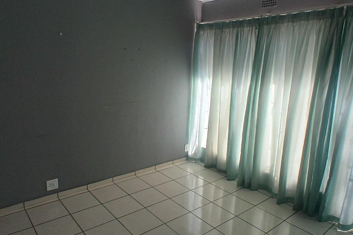An empty living room featuring tiled flooring and a large sliding glass door with curtains, providing natural light and access to the exterior.