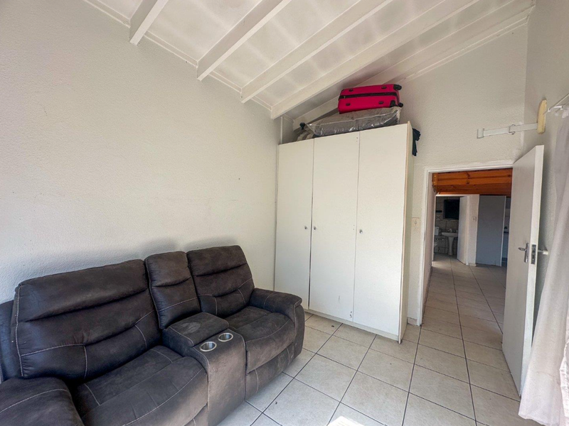 A bedroom featuring tiled flooring, a built-in wardrobe, and an exposed beam ceiling, providing a functional space with potential for cosmetic updates.
