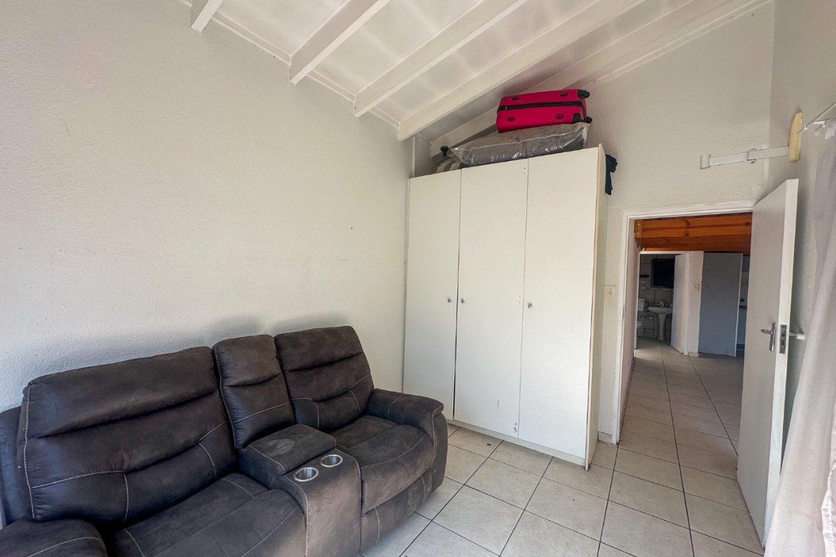 A bedroom featuring tiled flooring, a built-in wardrobe, and an exposed beam ceiling, providing a functional space with potential for cosmetic updates.