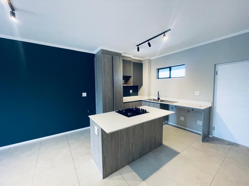 Modern kitchen featuring a central island with a built-in hob, sleek cabinetry, stone countertops, and contemporary track lighting in an open-plan layout.