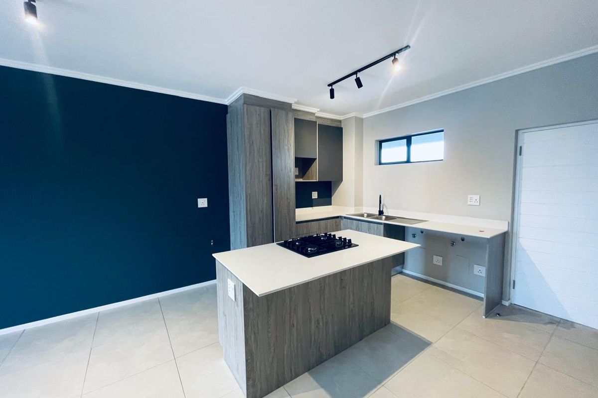 Modern kitchen featuring a central island with a built-in hob, sleek cabinetry, stone countertops, and contemporary track lighting in an open-plan layout.