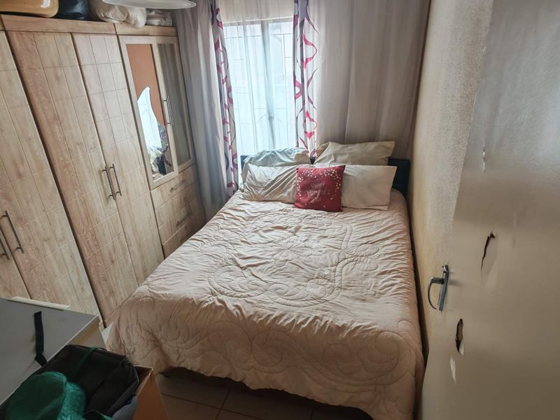 A compact bedroom featuring built-in wooden wardrobes and tiled flooring, requiring minor repairs to the door finish.