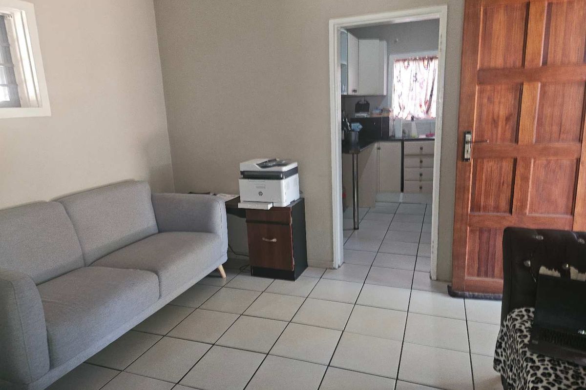 A living area with tiled flooring and a wooden door, providing a view into the adjacent kitchen space.