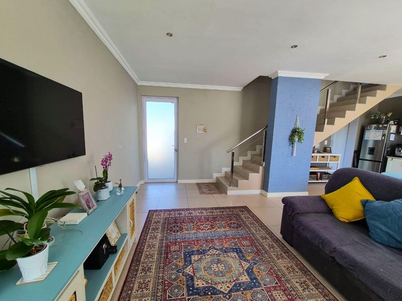 A bright living area featuring tiled floors, a modern staircase with stainless steel railings, and a frosted glass entrance door.