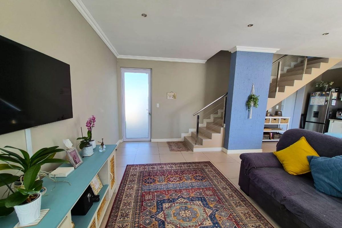 A bright living area featuring tiled floors, a modern staircase with stainless steel railings, and a frosted glass entrance door.