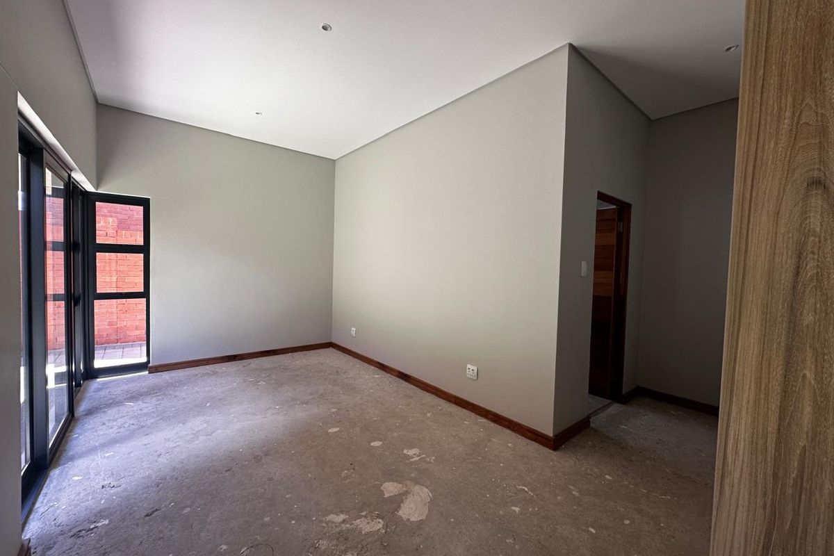 An empty bedroom featuring neutral walls, dark wood skirting boards, and large glass sliding doors leading to an outdoor area.