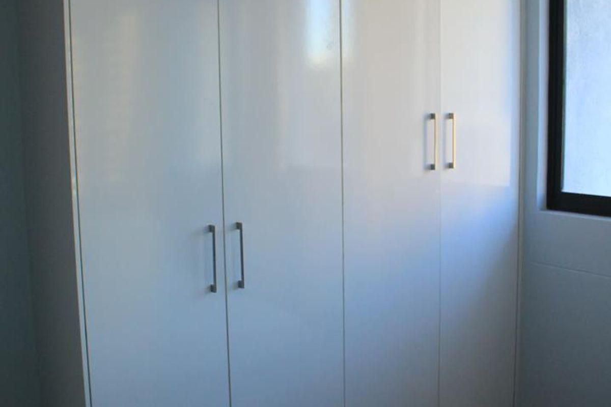 A bedroom featuring a modern, white high-gloss built-in wardrobe with sleek metal handles and a window.