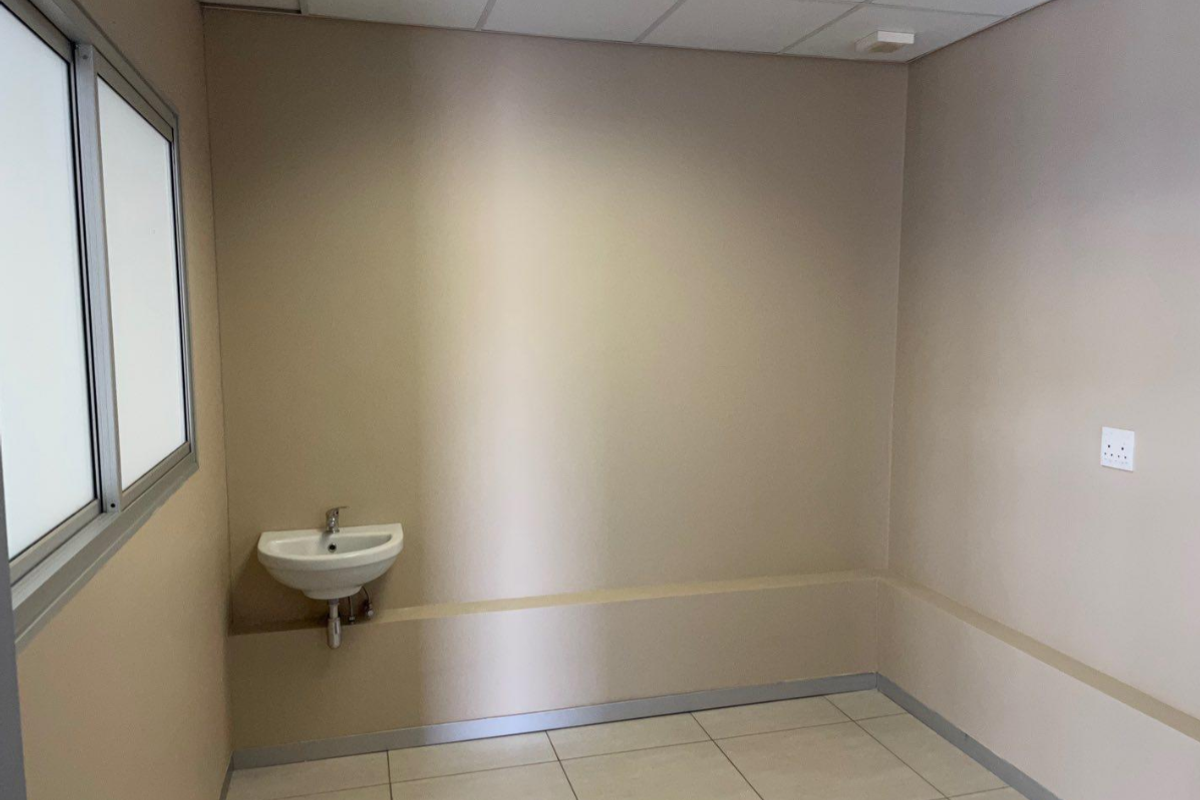 A clean, empty office space featuring neutral walls, tiled flooring, a suspended ceiling, and a convenient wall-mounted basin.