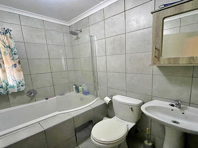 A functional bathroom featuring a bathtub with a shower screen, pedestal basin, and wall-mounted medicine cabinet, finished with neutral wall tiling.