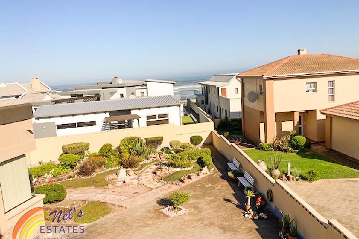 Elevated view of a residential property featuring a landscaped garden, paved courtyard, and surrounding coastal neighborhood with ocean views.
