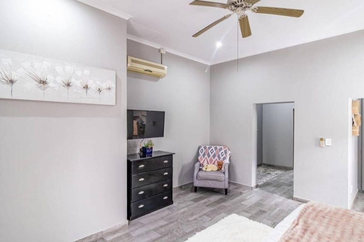 A well-maintained bedroom featuring neutral wall tones, laminate flooring, a ceiling fan, and a wall-mounted air conditioning unit.