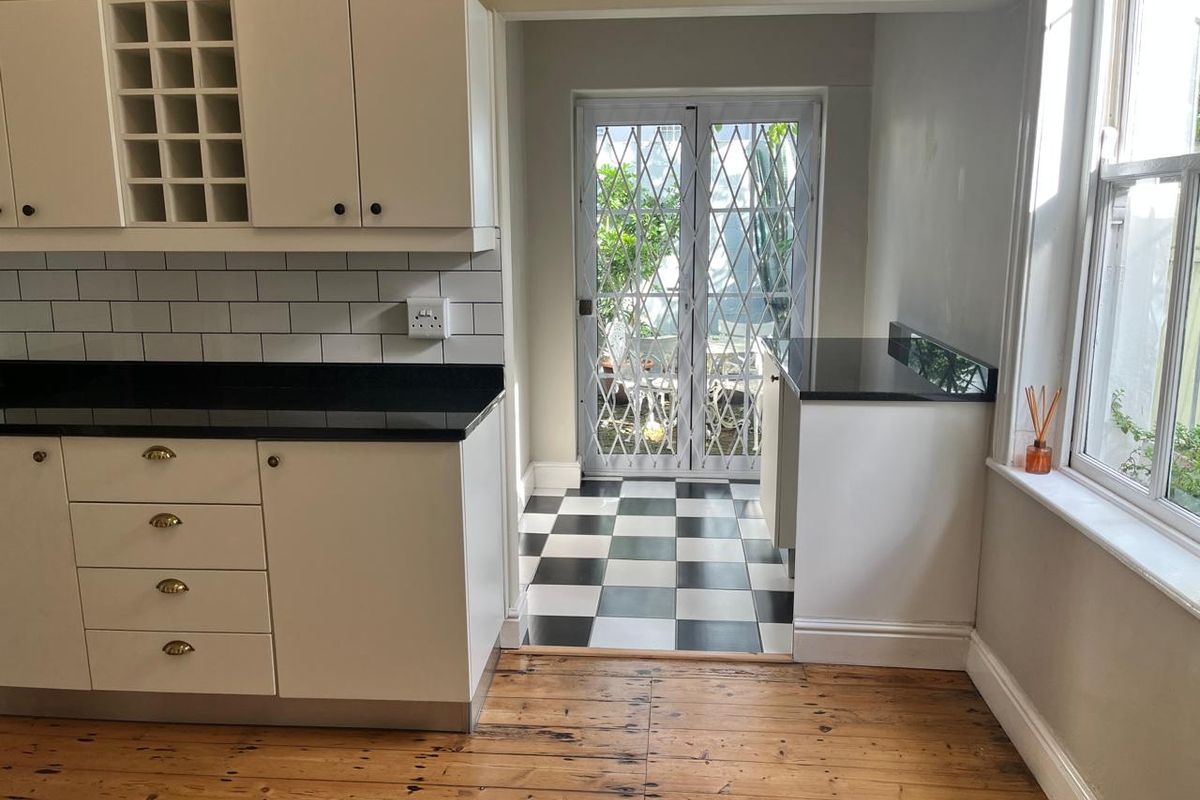 A bright kitchen featuring white cabinetry, black countertops, subway tile backsplash, and a checkerboard tiled transition area leading to a secure glass door.