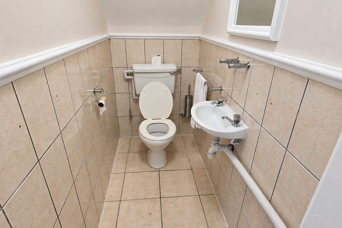 A compact powder room featuring a toilet, wall-mounted basin, and neutral ceramic tiling throughout.