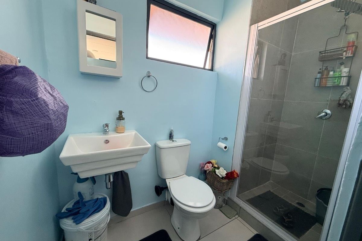 A functional bathroom featuring a wall-mounted basin, a standard toilet, and a glass-enclosed shower with tiled finishes.