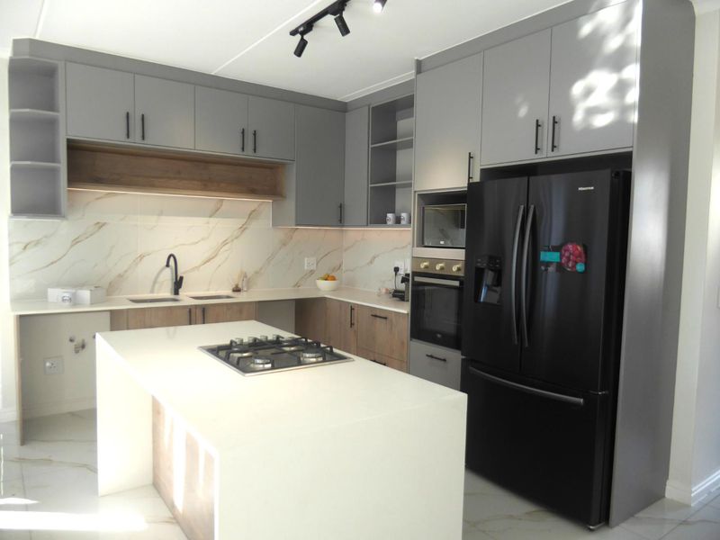 Modern kitchen featuring a central island with gas hob, stone countertops, marble-look splashback, and integrated appliances with sleek grey and wood-tone cabinetry.