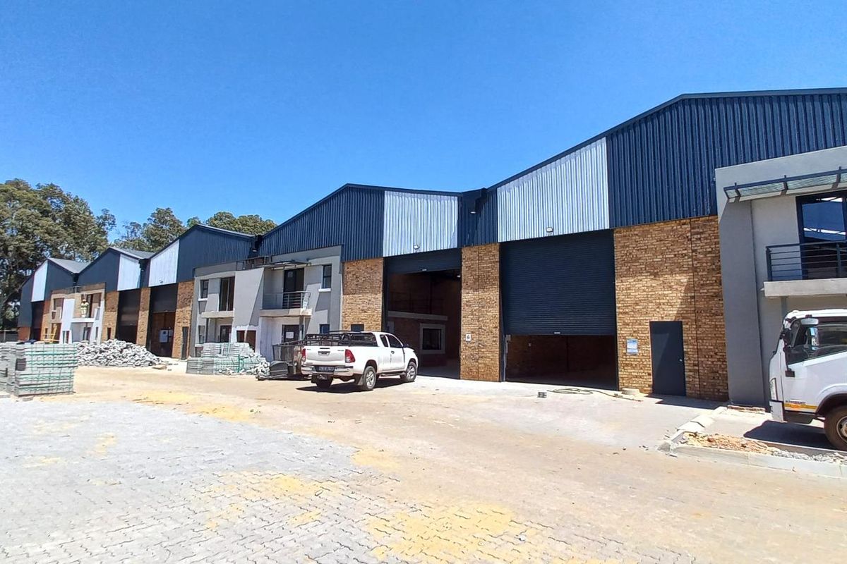 Front elevation of an industrial warehouse complex featuring multiple roller shutter doors, face brick and metal cladding finishes, and a paved yard area.