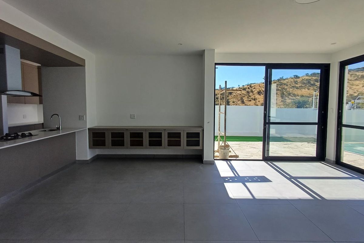 Modern open-plan kitchen and living area featuring sleek cabinetry, stone countertops, and large sliding doors opening to a patio and pool area.