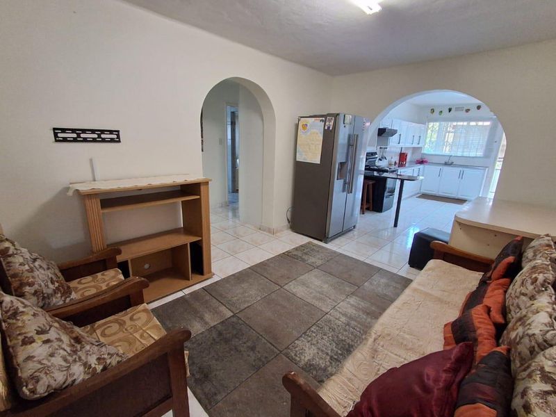 Open plan living area featuring tiled floors and an arched transition into a functional kitchen with built-in cabinetry and appliances.