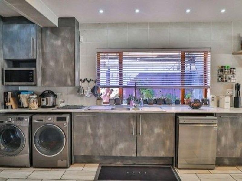 A functional kitchen featuring modern grey cabinetry, tiled flooring, integrated dishwasher, and ample counter space with a tiled backsplash and recessed lighting.
