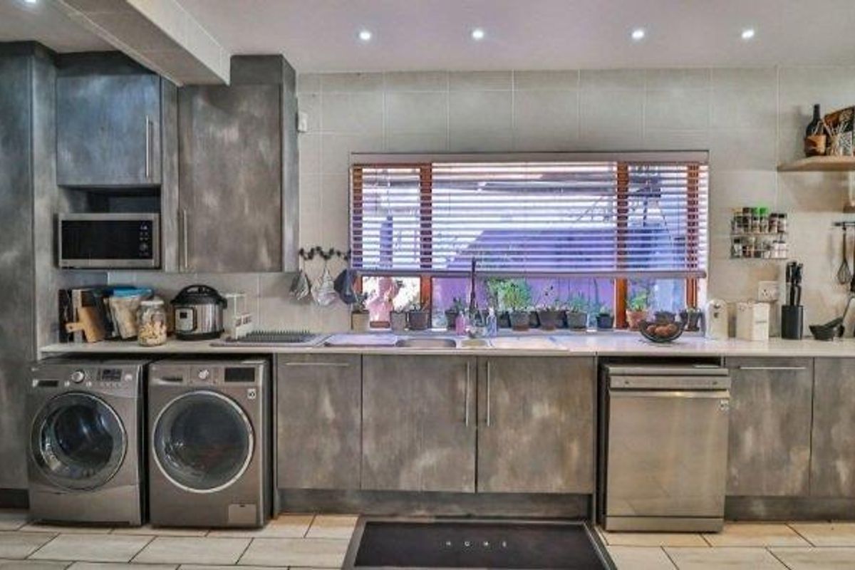 A functional kitchen featuring modern grey cabinetry, tiled flooring, integrated dishwasher, and ample counter space with a tiled backsplash and recessed lighting.