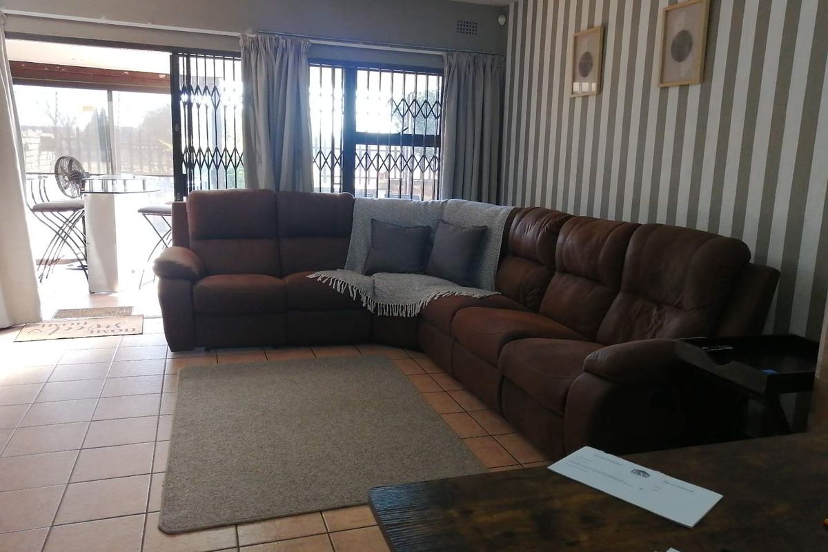 A living room featuring tiled flooring and a sliding glass door with security gate, providing access to an outdoor patio area.