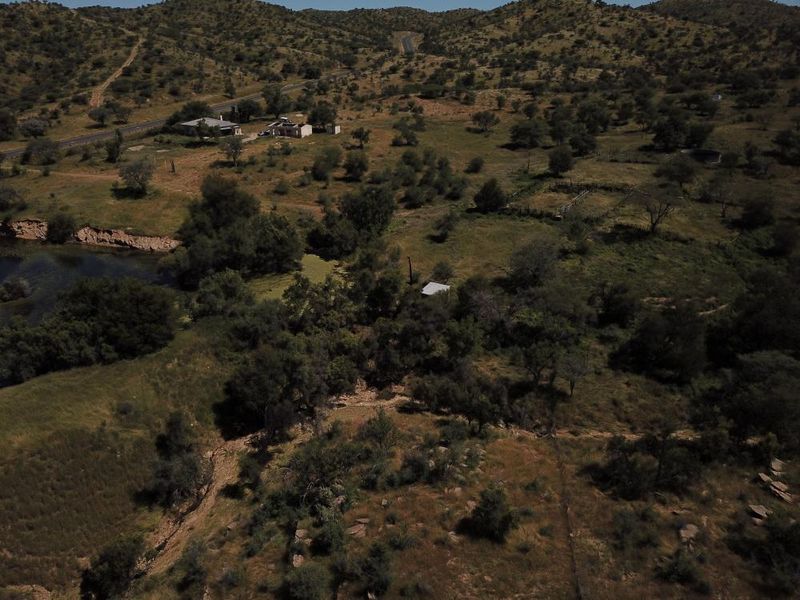 An aerial view of a rural property featuring expansive natural landscape, indigenous vegetation, and proximity to a water body and access road.