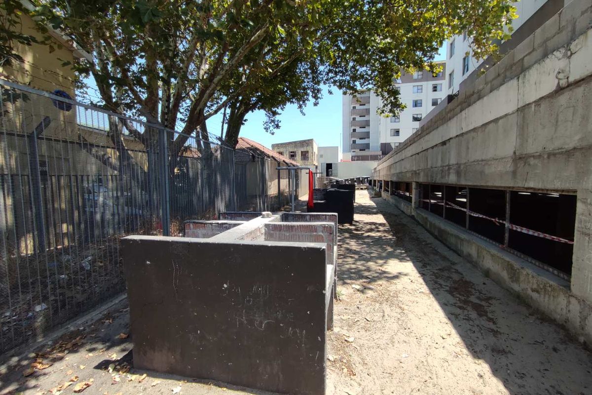 An outdoor area featuring concrete structures and a metal security fence, currently in a raw, unfinished state with unpaved ground.
