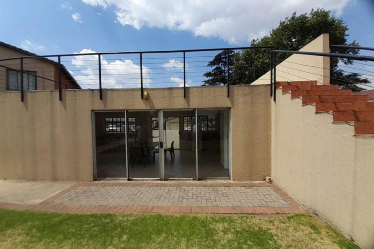Rear view of the townhouse featuring a paved patio area, sliding glass doors, and an elevated terrace with metal railing.