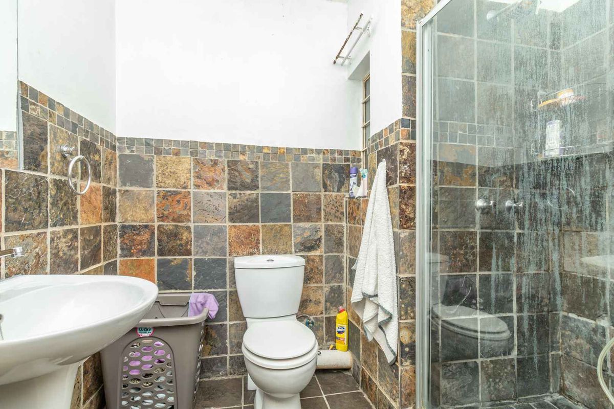 A compact bathroom featuring a shower enclosure, pedestal basin, and toilet with dated slate-style wall tiling.
