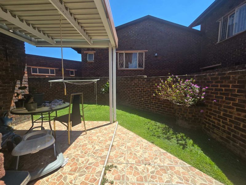 A private outdoor patio area featuring a covered roof, tiled flooring, and a small garden space enclosed by brick boundary walls.