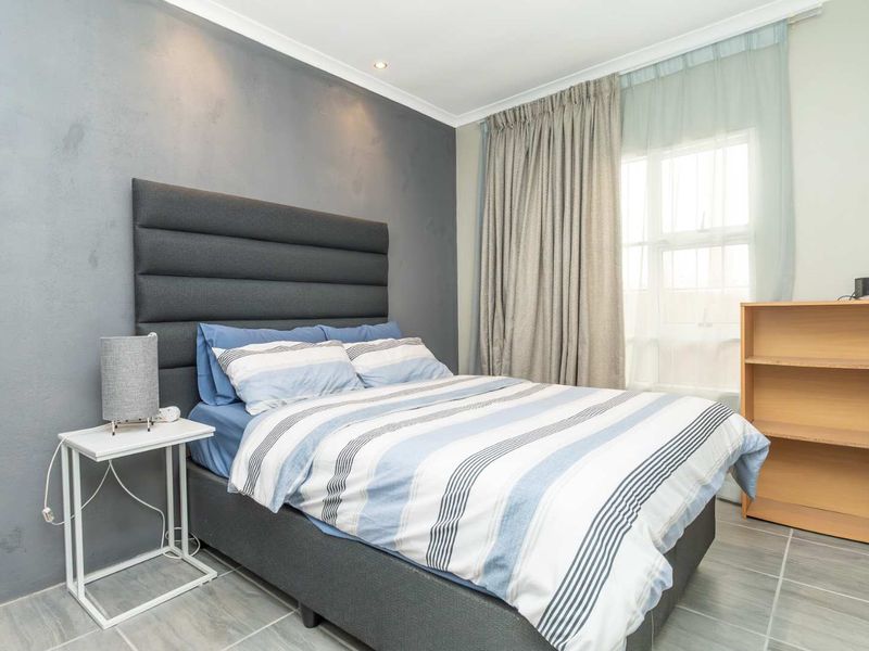 A well-lit bedroom featuring tiled flooring, a feature wall, and large windows with curtains, providing a comfortable and functional living space.