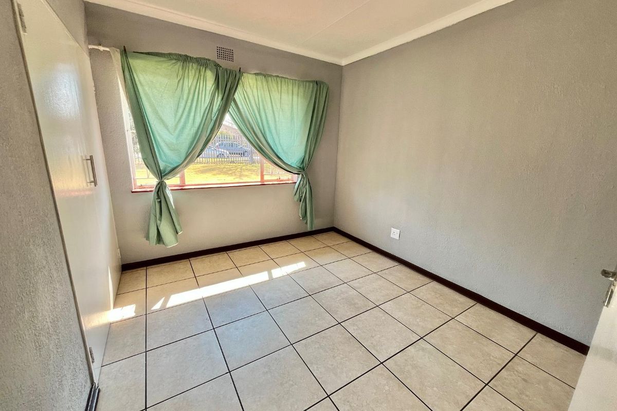 A bright, empty bedroom featuring neutral grey walls, tiled flooring, and a built-in cupboard, offering a clean and versatile space.