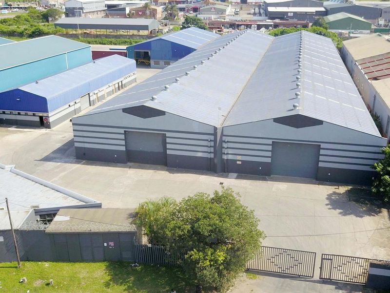 Aerial view of an industrial warehouse complex featuring dual roller shutter doors, metal roofing, and a paved yard area with perimeter security fencing.