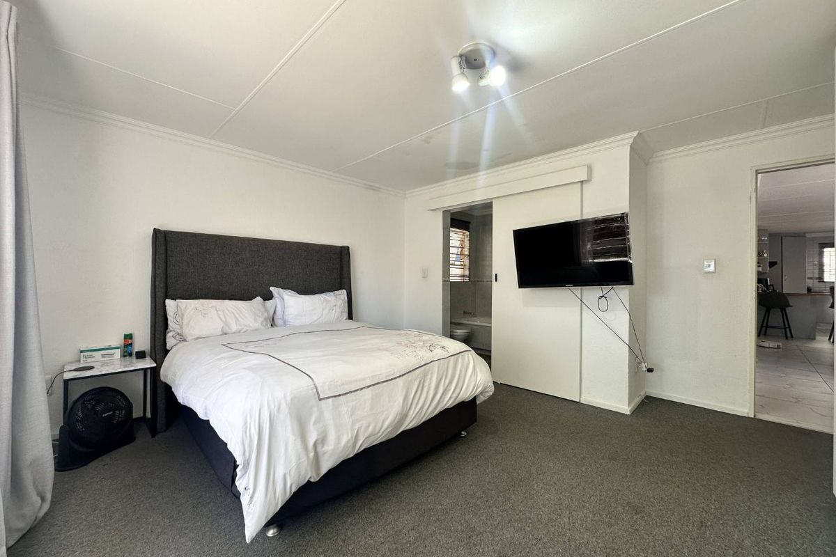 Spacious bedroom featuring neutral carpeting, a sliding door leading to an en-suite bathroom, and direct access to the adjacent living area.