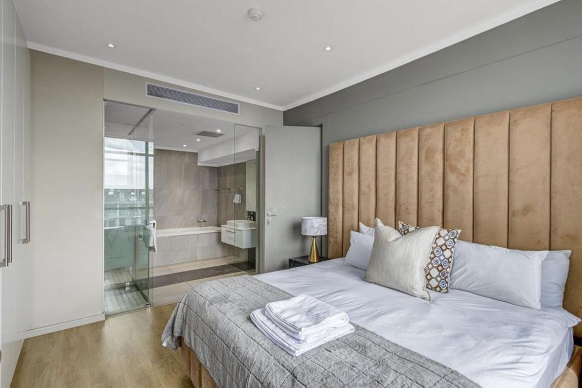 Modern bedroom featuring an integrated glass-enclosed en-suite bathroom with contemporary fixtures, recessed lighting, and neutral finishes.