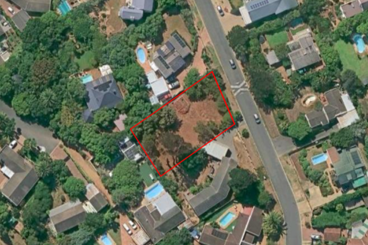 Aerial view of a vacant residential plot highlighted in red, situated within an established suburban neighborhood with mature trees and surrounding homes.