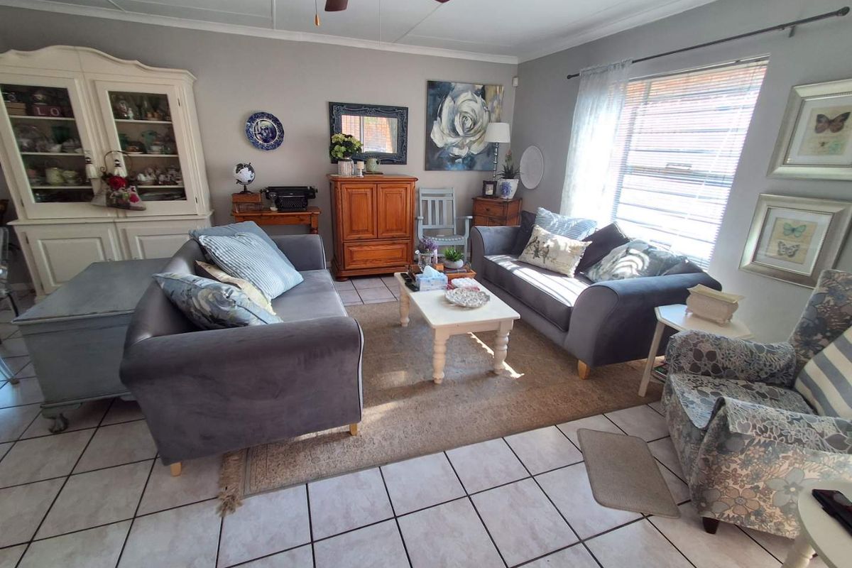 A comfortable living room featuring tiled flooring, a ceiling fan, and large windows with blinds, providing a bright and functional space for relaxation.