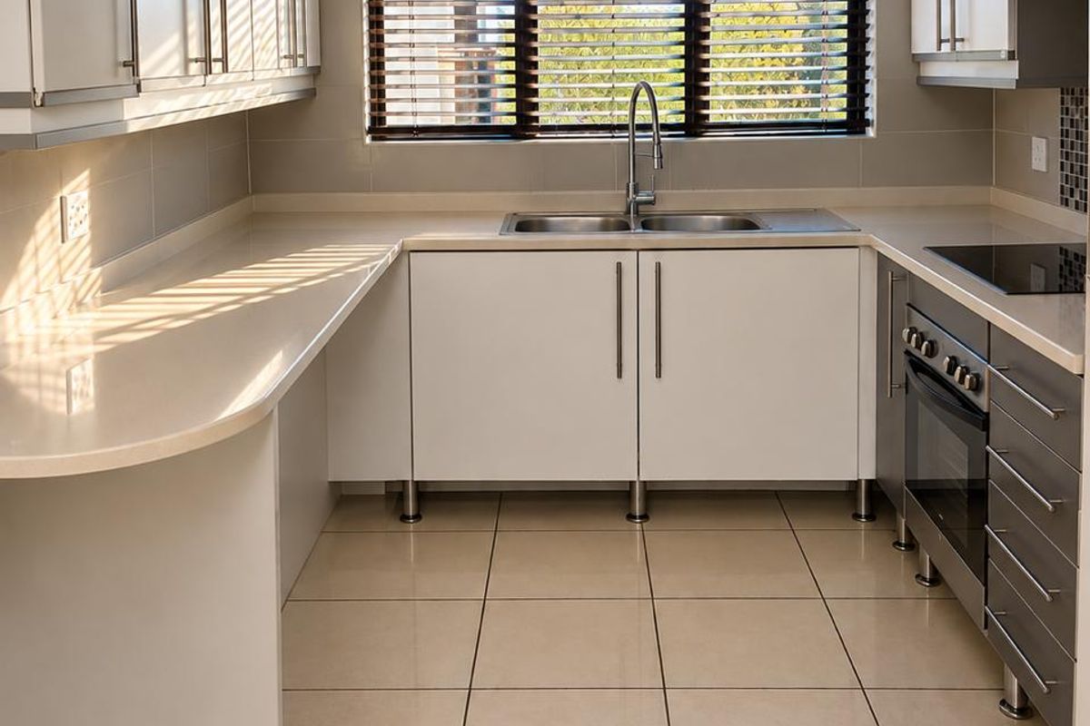 A clean, modern kitchen featuring white cabinetry, stone countertops, integrated appliances, and tiled flooring, offering a functional and well-maintained workspace.