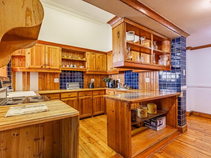A traditional kitchen featuring extensive timber cabinetry, wooden countertops, and a blue tiled splashback, offering a warm, rustic aesthetic with functional storage.
