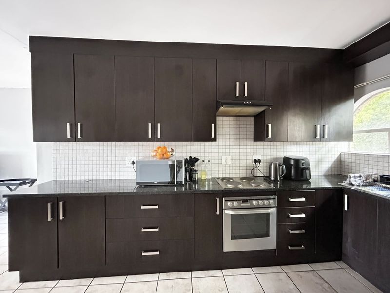 A functional kitchen featuring dark wood cabinetry, granite countertops, a tiled backsplash, and integrated stainless steel appliances.