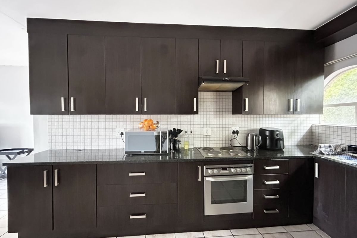 A functional kitchen featuring dark wood cabinetry, granite countertops, a tiled backsplash, and integrated stainless steel appliances.