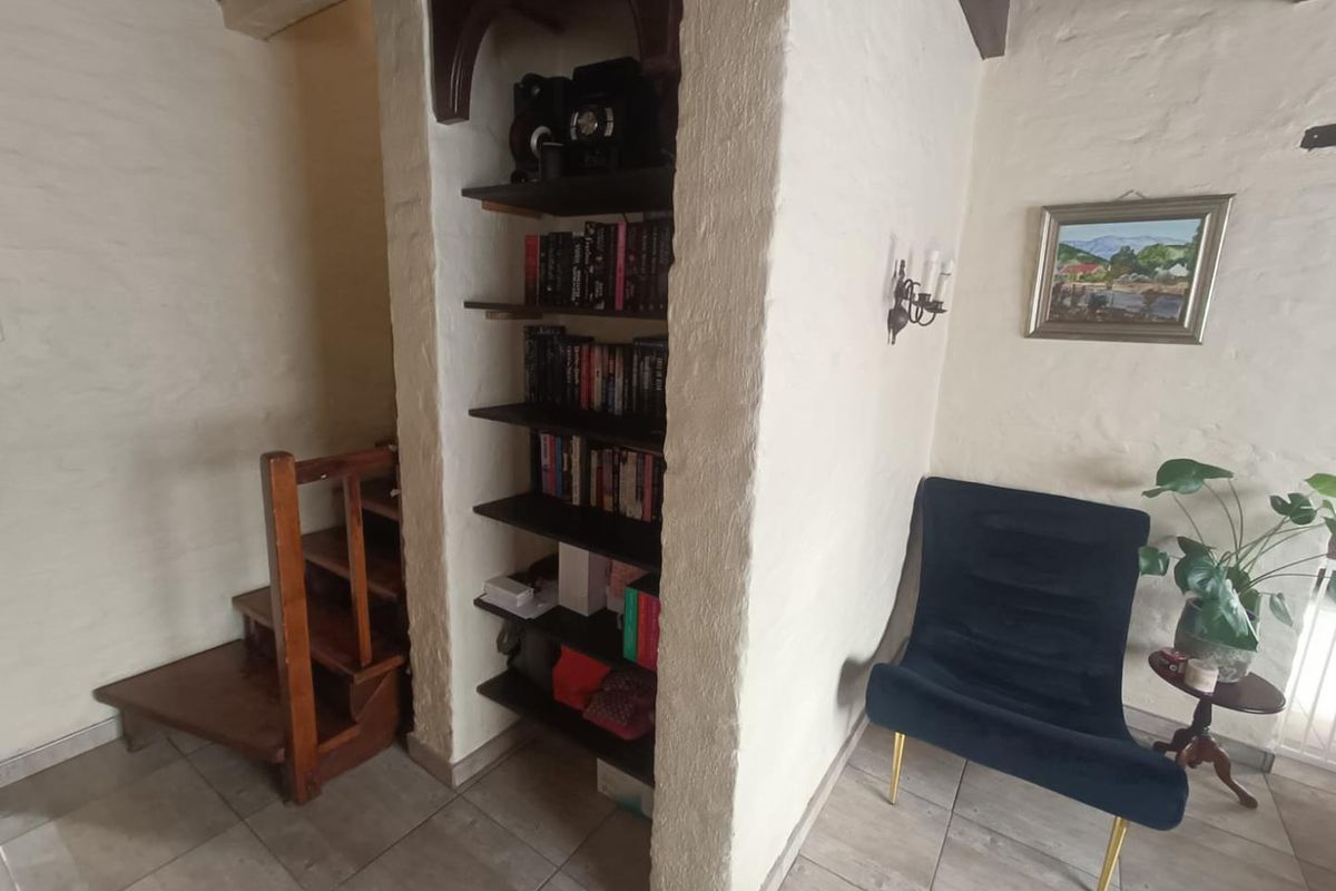 A rustic interior space featuring a built-in arched bookshelf, wooden staircase, and textured walls with tiled flooring.