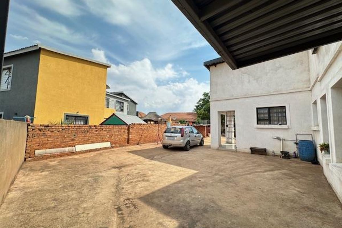 A spacious paved rear courtyard area featuring a covered patio section, brick boundary walls, and direct access to the main building structure.