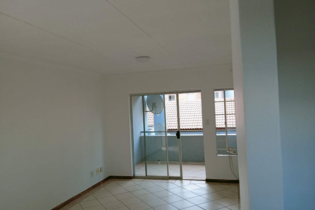 A bright, empty living area featuring tiled flooring and sliding glass doors that open onto a private balcony.