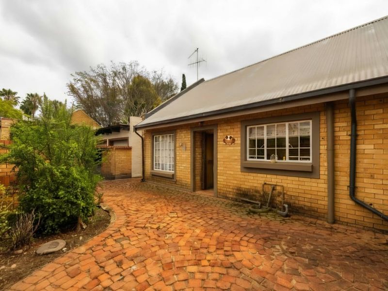 A rear exterior view of a brick house featuring a corrugated metal roof and a paved courtyard area.