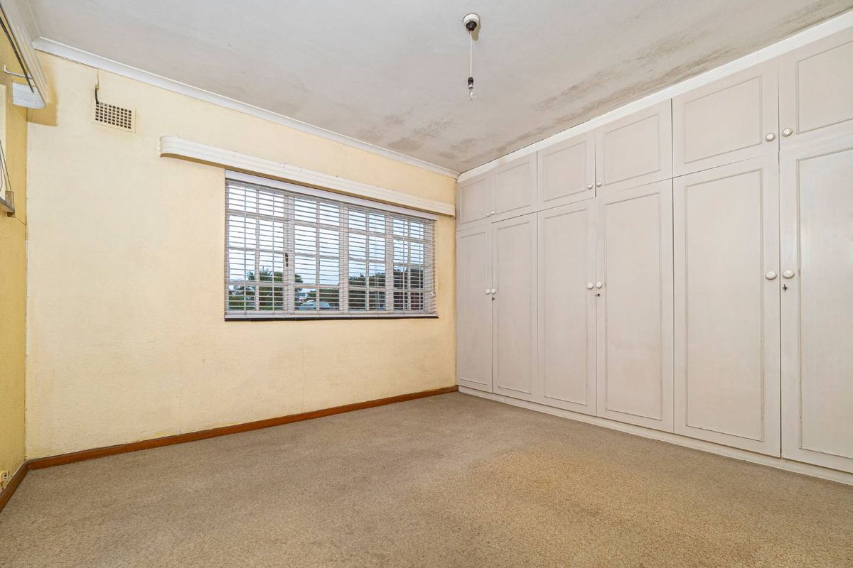 A bedroom featuring built-in floor-to-ceiling cabinetry, carpeted flooring, and a window with fitted blinds.